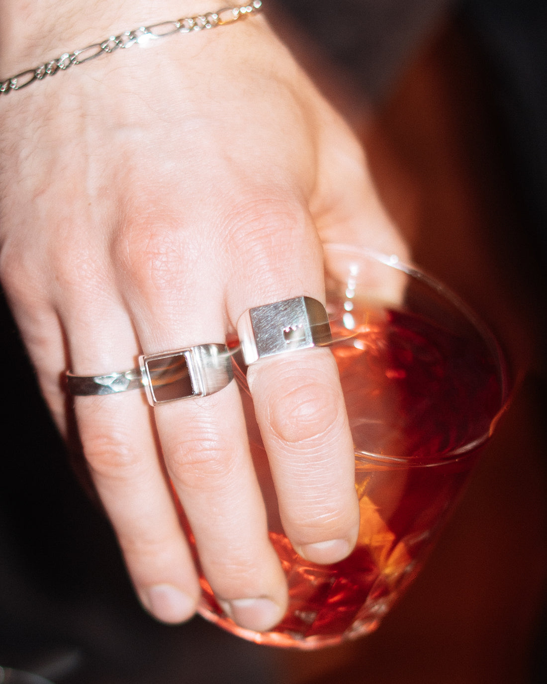 Crown Signet Ring - stacked with Onyx Signet Ring and Hammered Band Ring, Figaro chain bracelet on wrist, hand holding cocktail