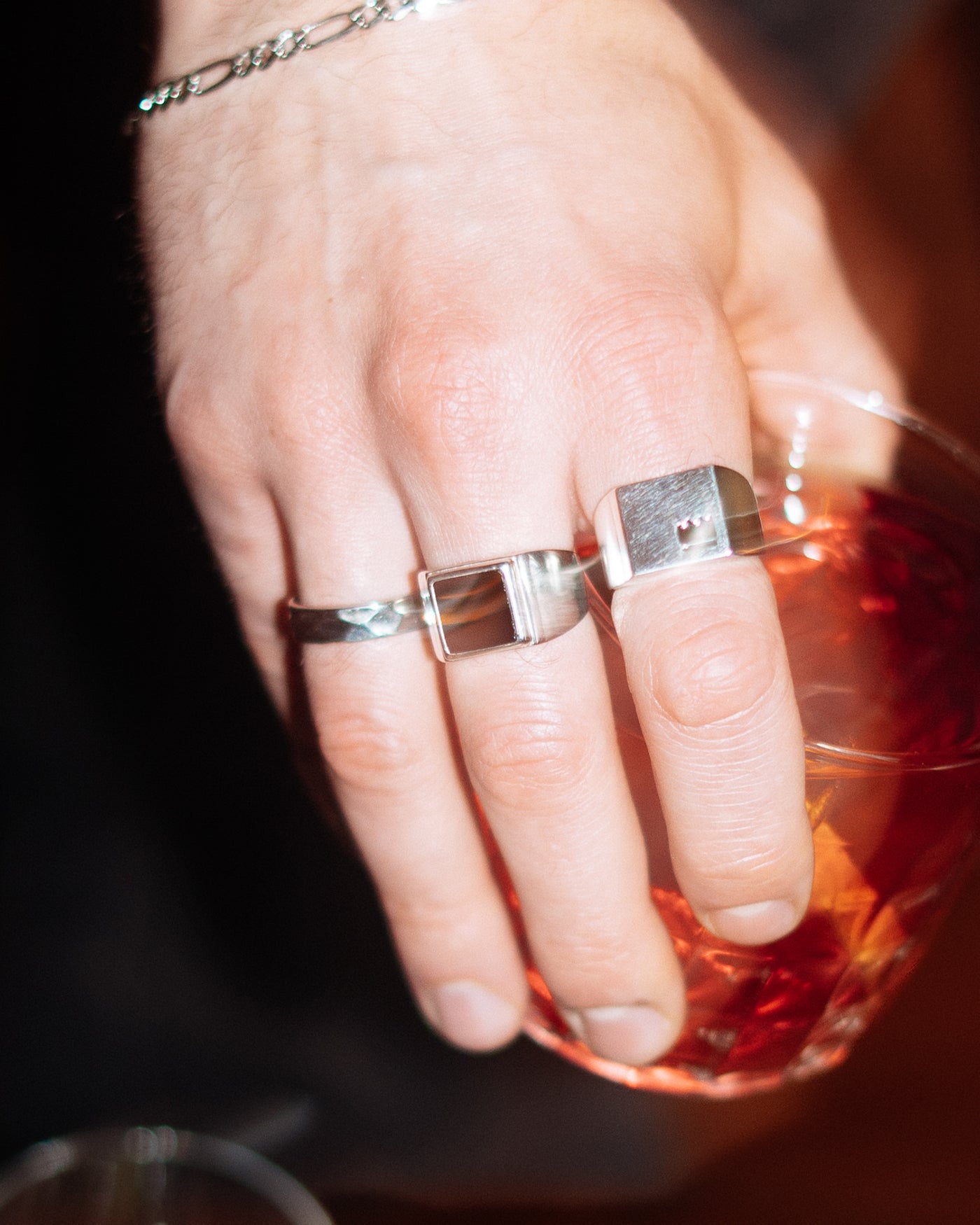 Onyx Signet Ring - stacked with Crown Signet Ring and Hammered Band Ring, Figaro chain bracelet on wrist, hand holding cocktail