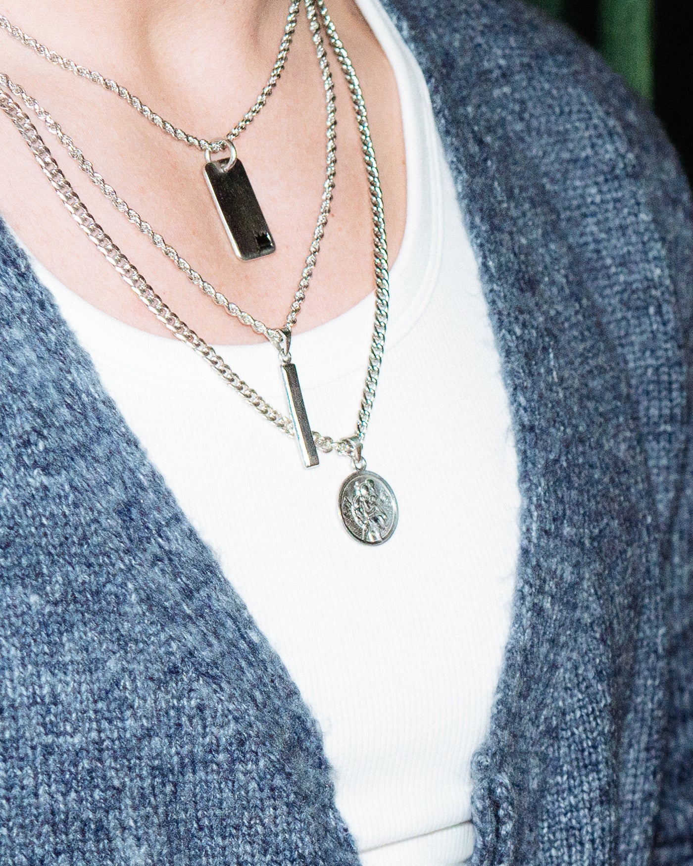 St Christopher Pendant - styled with Crown Dog Tag, Plain Dog Tag and Totem Pendant, layered chains worn at neckline against blue cardigan and white t-shirt