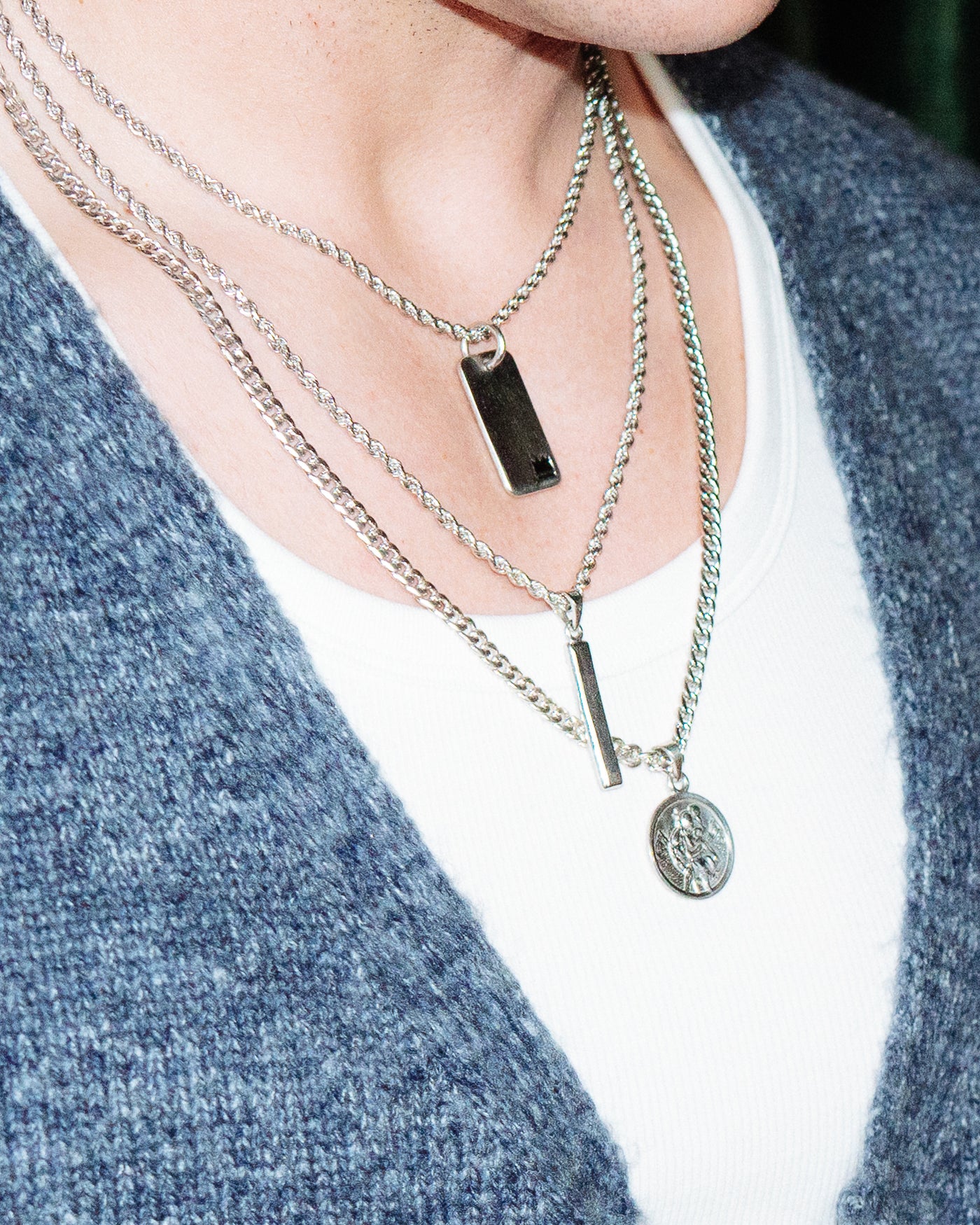 Crown Dog Tag - styled with Plain Dog Tag, St Christopher Pendant and Totem Pendant, layered chains worn at neckline against blue cardigan and white t-shirt