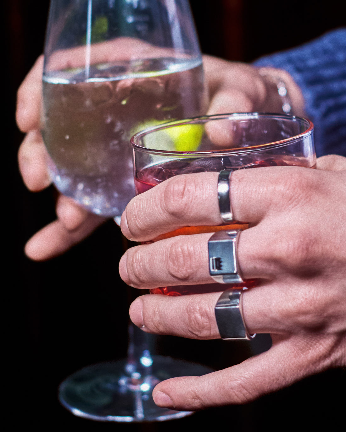 Plain Signet Ring - stacked with Crown Signet Ring and Plain Band Ring, two hands holding cocktail glasses, dark editorial setting