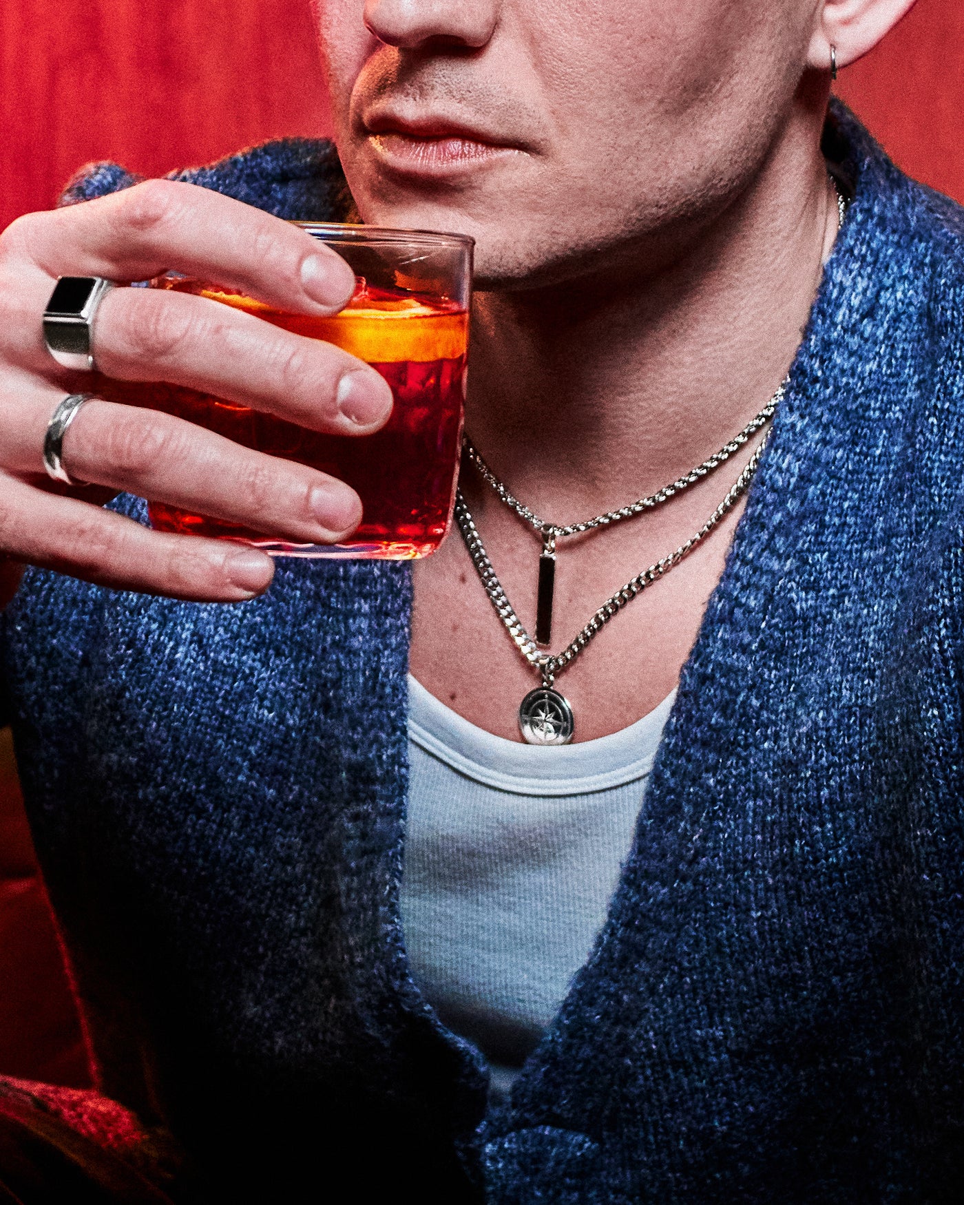 Totem Pendant - styled with Onyx Signet Ring, Hammered Band Ring and Compass Pendant, Figaro chain bracelet on wrist, model in blue cardigan holding negroni