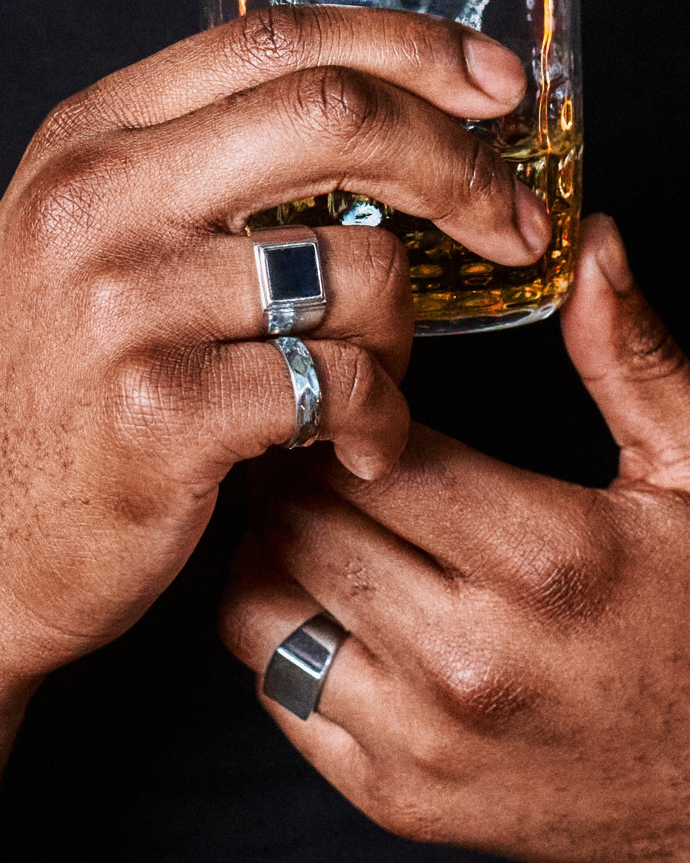 Onyx Signet Ring - stacked with Hammered Band Ring and Plain Signet Ring, two hands holding whisky glass, dark editorial close-up